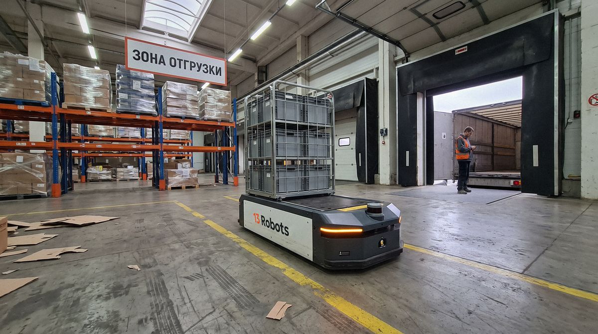 Колёсная платформа 13 Robots везёт тележку с ящиками в зоне отгрузки, у ворот кладовщик сверяет груз